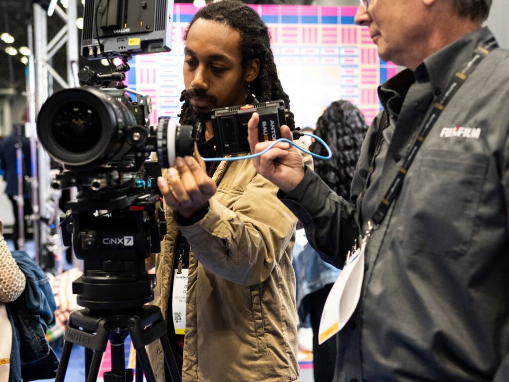 Two men are working a broadcast camera on the show floor.