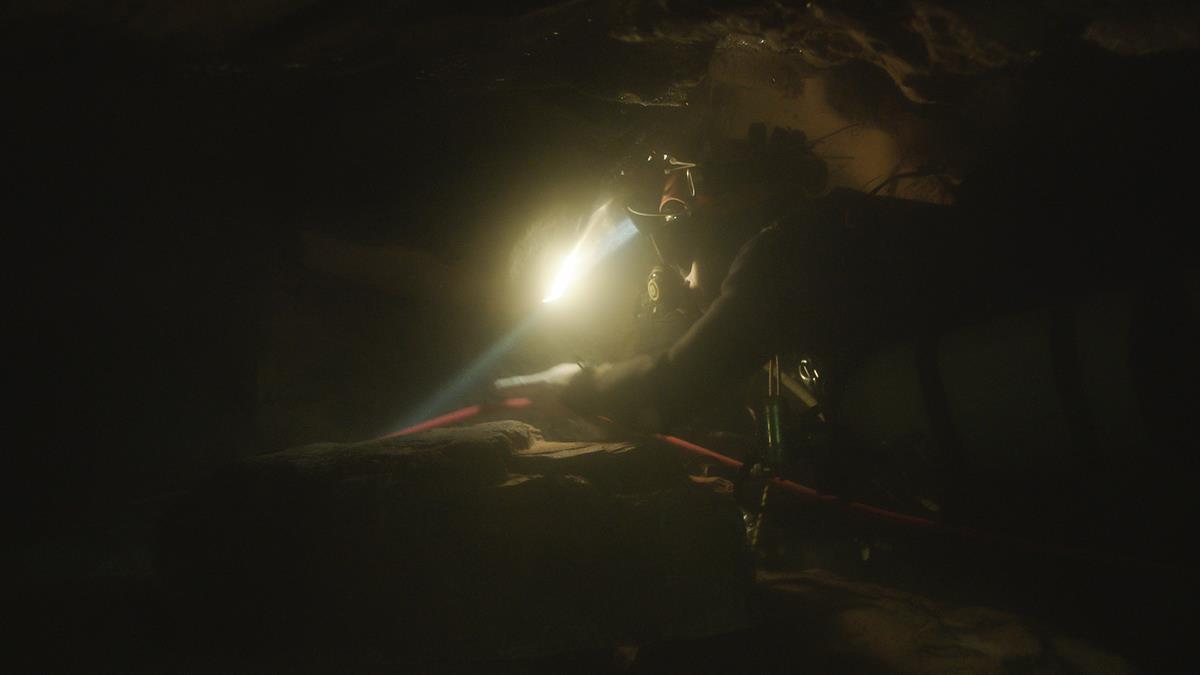 A diver swims through a dark cave guided by a headlamp in “The Rescue.” Cr: National Geographic