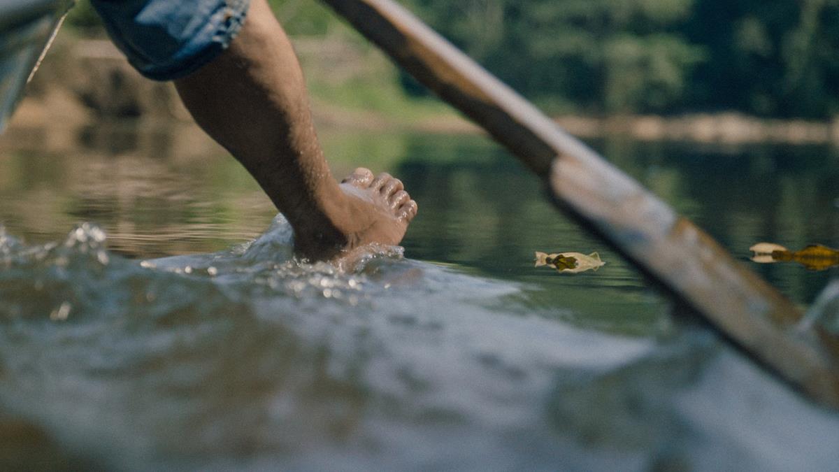Bitaté Uru-eu-wau-wau hangs his foot out of the boat while fishing in his community's protected Indigenous territory in Rondônia, Brazil. Cr: Alex Pritz/Amazon Land Documentary