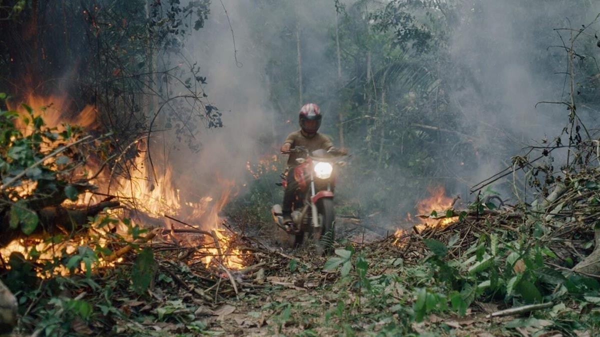 An invader rides his motorcycle through the rainforest fire blaze. Cr: Alex Pritz/Amazon Land Documentary